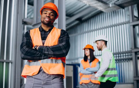 Three factory workers in safety hats discussing manufacture plan